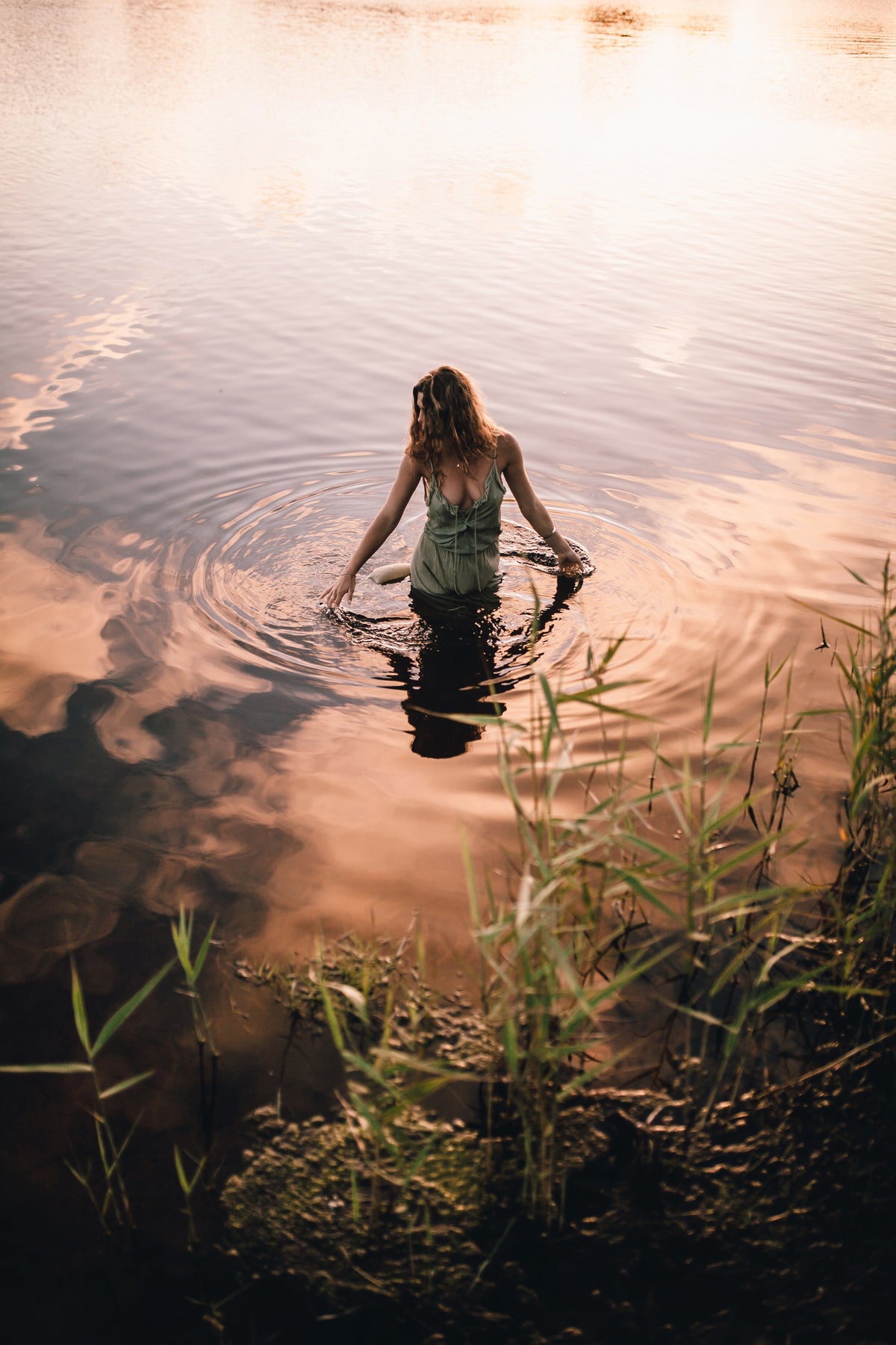 Woman wearing a lacey maxi dress standing in the water with both her hands touching the water