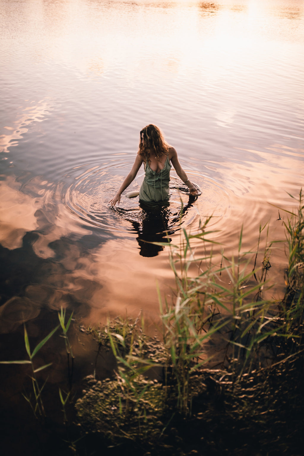 Woman wearing a lacey maxi dress standing in the water with both her hands touching the water