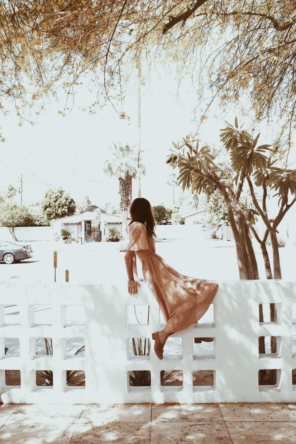 Back view of a woman wearing toasted peach maxi dress sitting on a white fence