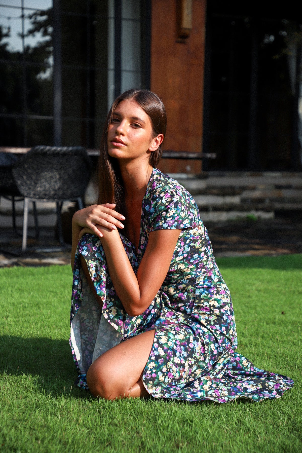 A woman sitting on grass wearing a floral maxi wrap dress with capped sleeves.