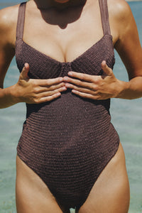 Woman's torso showing her wearing brown one piece bathing suit
