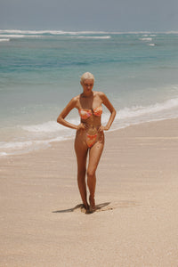 woman standing in the beach sand wearing a colourful bikini