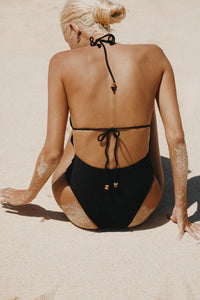 Blonde haired woman on a beach wearing black halter neck one piece bathing suit