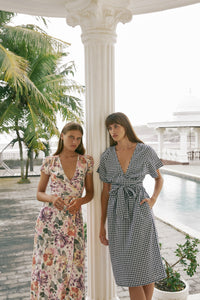 Two women leaning on a porch post wearing maxi floral and gingham midi dress