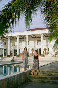 Farther view of two women wearing gingham dress and black top with floral midi skirt standing next to a pool