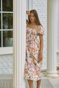 Woman leaning on a front porch post wearing rosy floral printed summer dress 