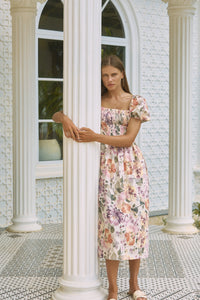 Woman hugging a front porch post wearing rosy floral printed summer dress 