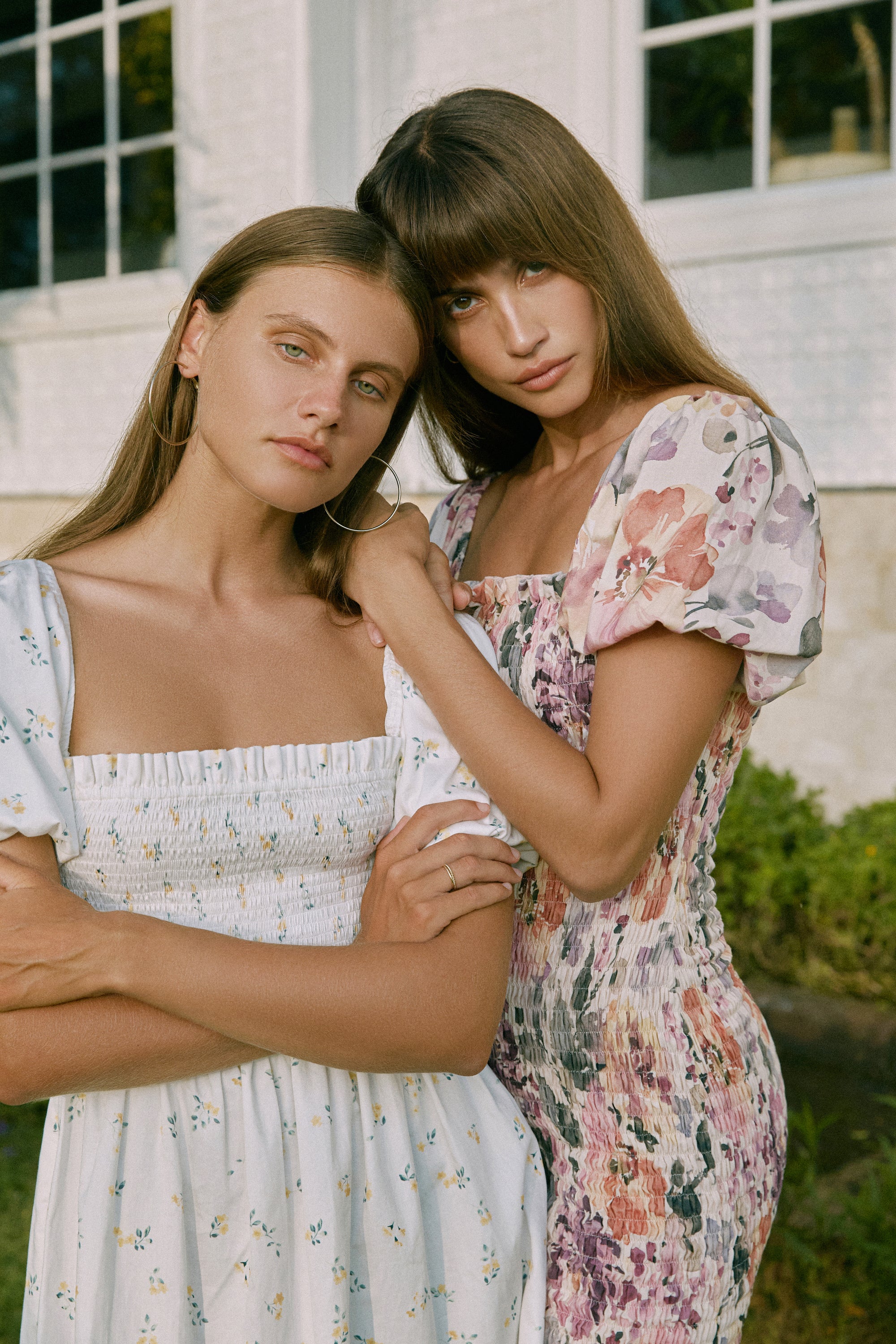 Closer view of two women wearing shirred floral print dresses standing in front of a window