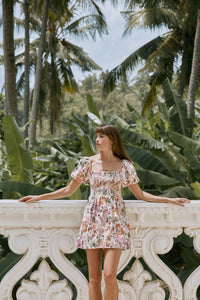 Woman wearing floral printed  summer dress leaning on a white balustrade