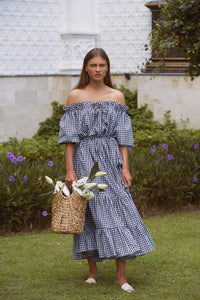 Woman wearing maxi gingham dress carrying a wicker basket with white flowers