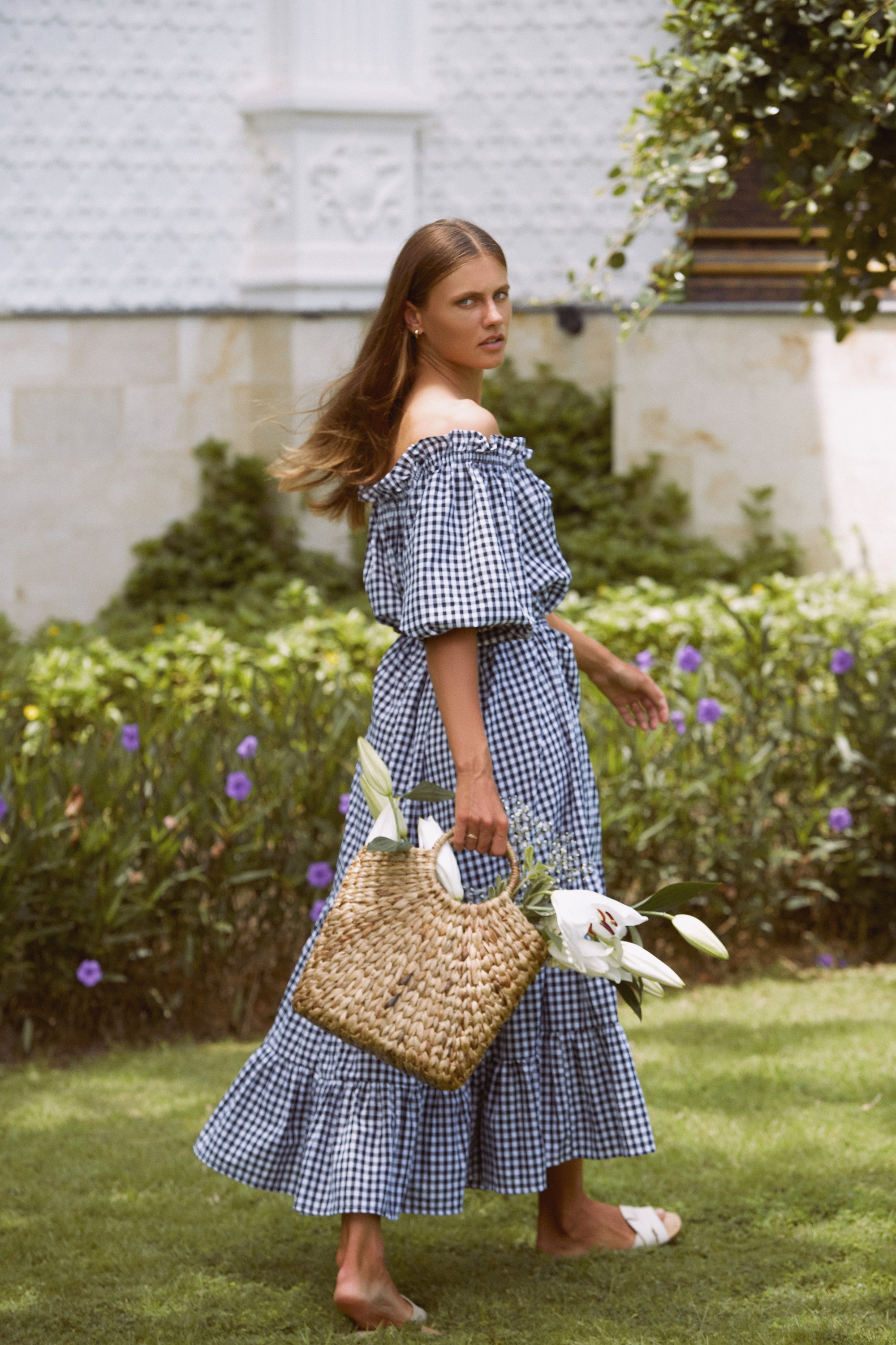 Woman in a maxi gingham dress carrying a wicker basket with white flowers