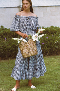Woman in a maxi gingham dress carrying basket with white flowers