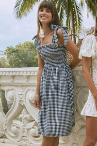 Woman wearing shoulder tie gingham midi dress standing in front of white balustrade