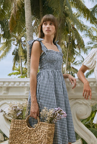 Woman wearing shoulder-tie gingham midi dress holding a basket with flowers
