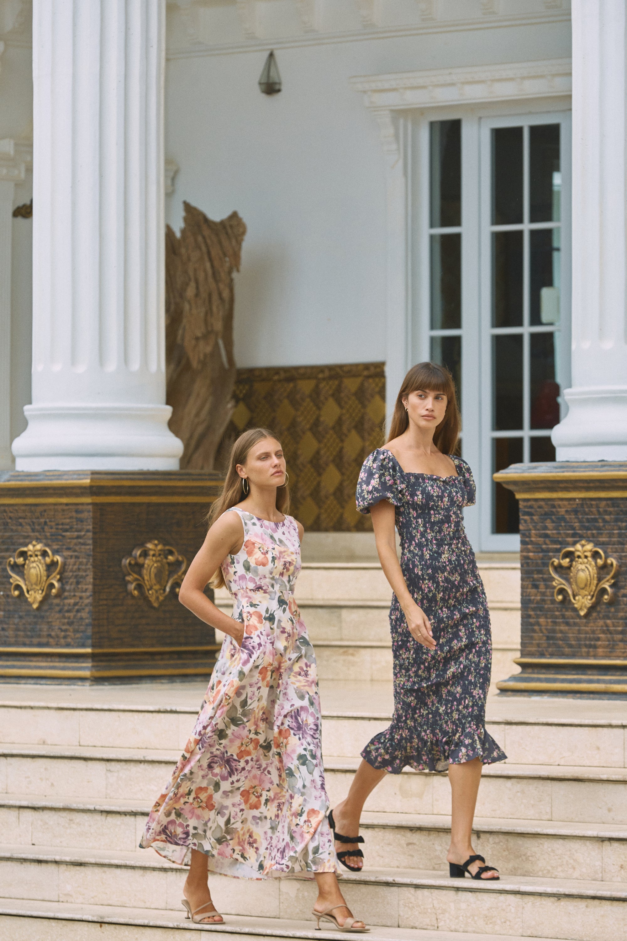 Two women walking side by side wearing floral print dresses 