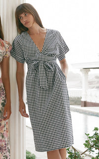 Woman leaning on a white porch post wearing black gingham tie-front midi dress