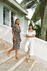 Two women wearing a wrap midi dress and a shirred puff sleeve top and white pants